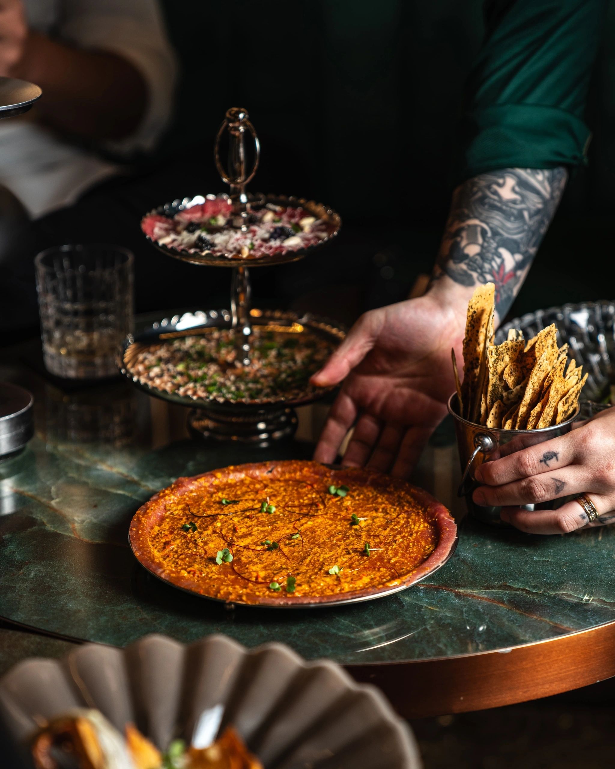 Dishes served on a green marble table at HUSH: a tiered silver stand and a plate with crisp flatbreads