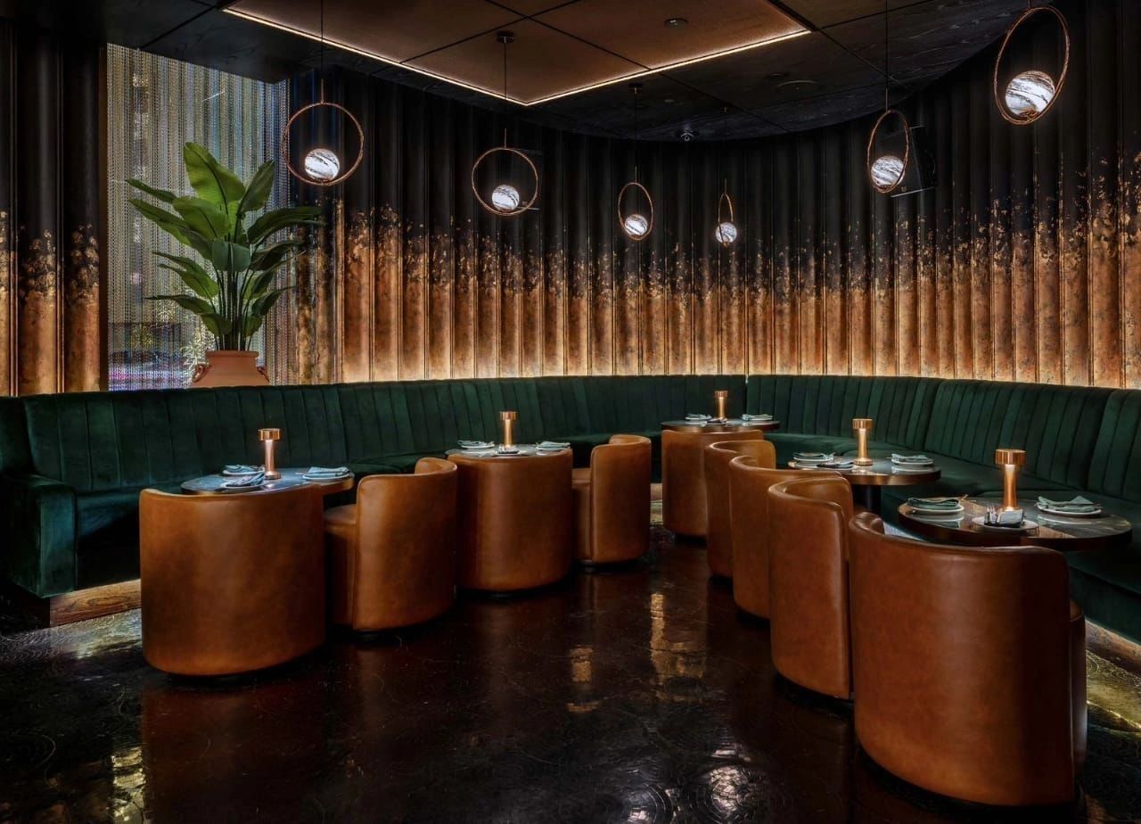 The lounge at HUSH: a curved green velvet banquette and cognac leather tub chairs beneath glowing globe pendants